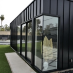 A dark metal-clad guest home with a long window wall onto a lawn